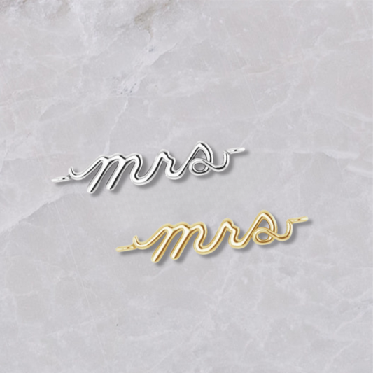 Permanent jewelry connectors with the word 'Mrs' shown in sterling silver and 14k yellow gold on a marble background. Perfect for newlyweds. 