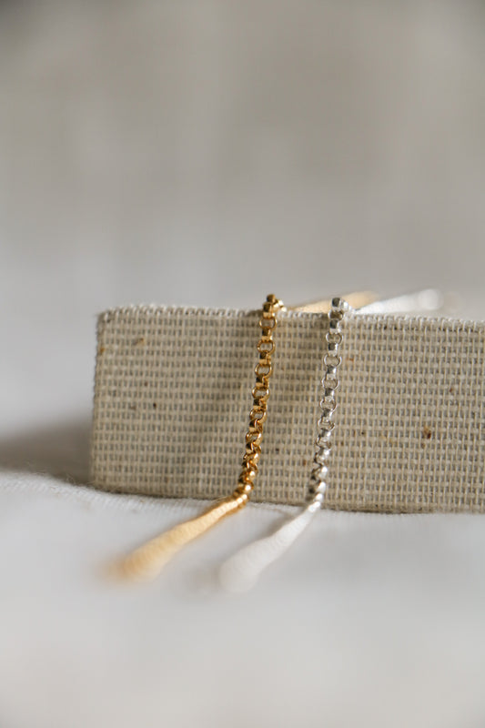 Gold-filled and sterling silver chains laying on a woven backdrop. Used as permanent bracelets, necklaces, and anklets at Charm City Links.