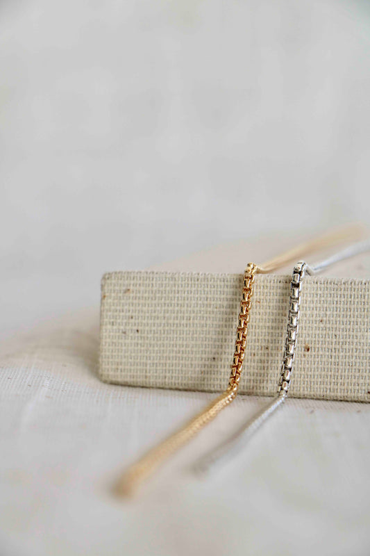 Gold-filled and sterling silver rounded box permanent jewelry links laying across a woven surface and linen background.