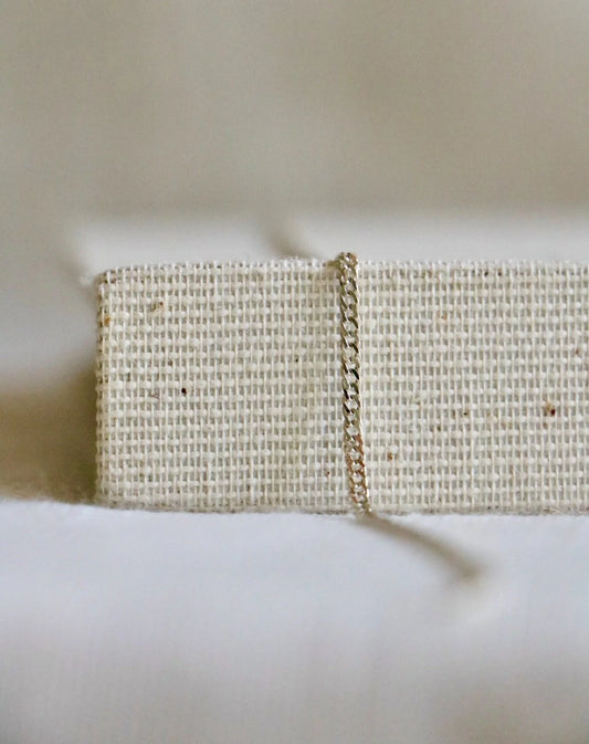 Sterling silver cuban link for permanent bracelets or necklaces on a light woven holder and blurred background. 