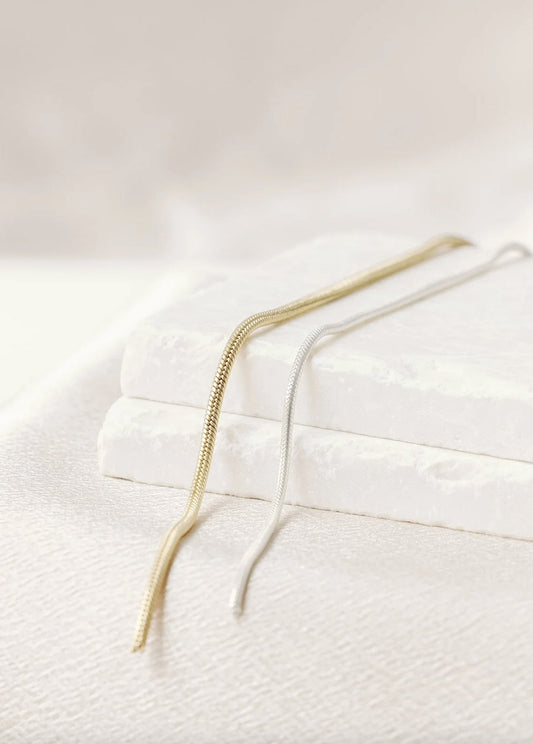 Gold-filled and sterling silver Snake Link chain. The chains are reminiscent of snake skin, and lay across an ivory background and stone blocks.