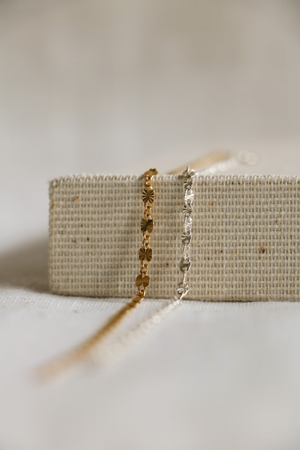 Gold-filled and sterling silver Starburst permanent jewelry links sitting on a woven background, with interchanging starburst gold links and chain links.