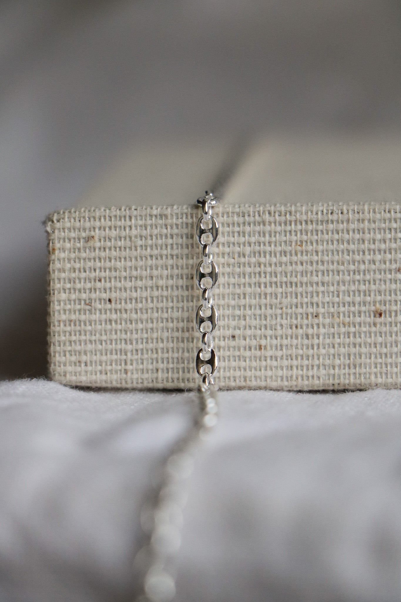 Close-up of a luxury permanent jewelry chain. Sterling silver thick chain laying on a woven jewelry holder, with the link called 'Gucci Link'. 