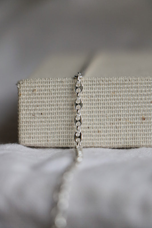 Close-up of a luxury permanent jewelry chain. Sterling silver thick chain laying on a woven jewelry holder, with the link called 'Gucci Link'. 