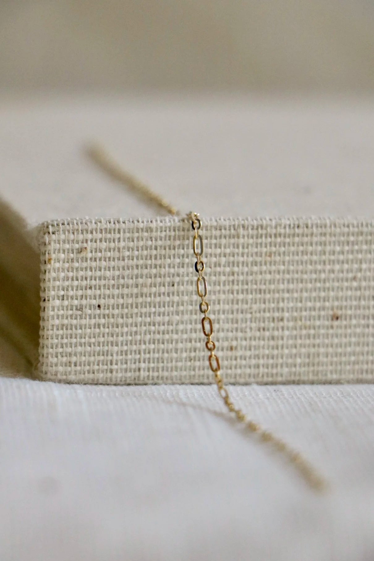 Permanent jewelry chain on a woven holder and light linen background. The link includes small and medium ovals in two-toned gold. 